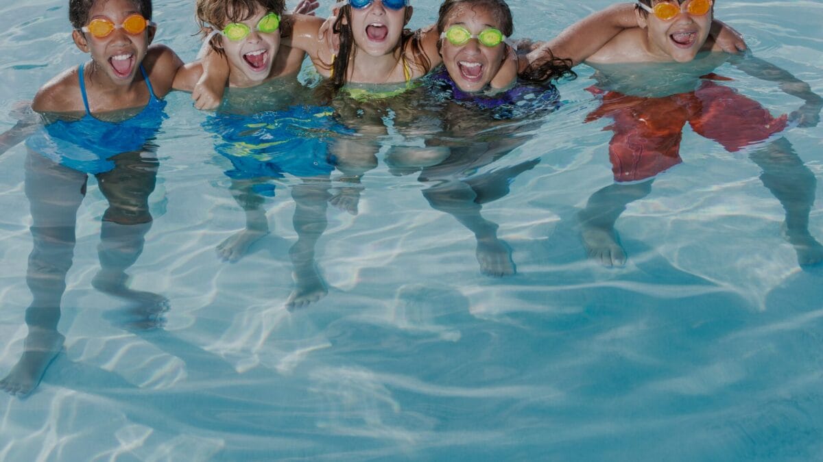 5 kids hugging standing next to each other inside the outdoor pool