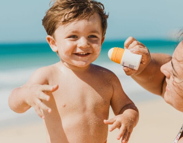 Photo of mom applying sunscreen on toddler by the beach